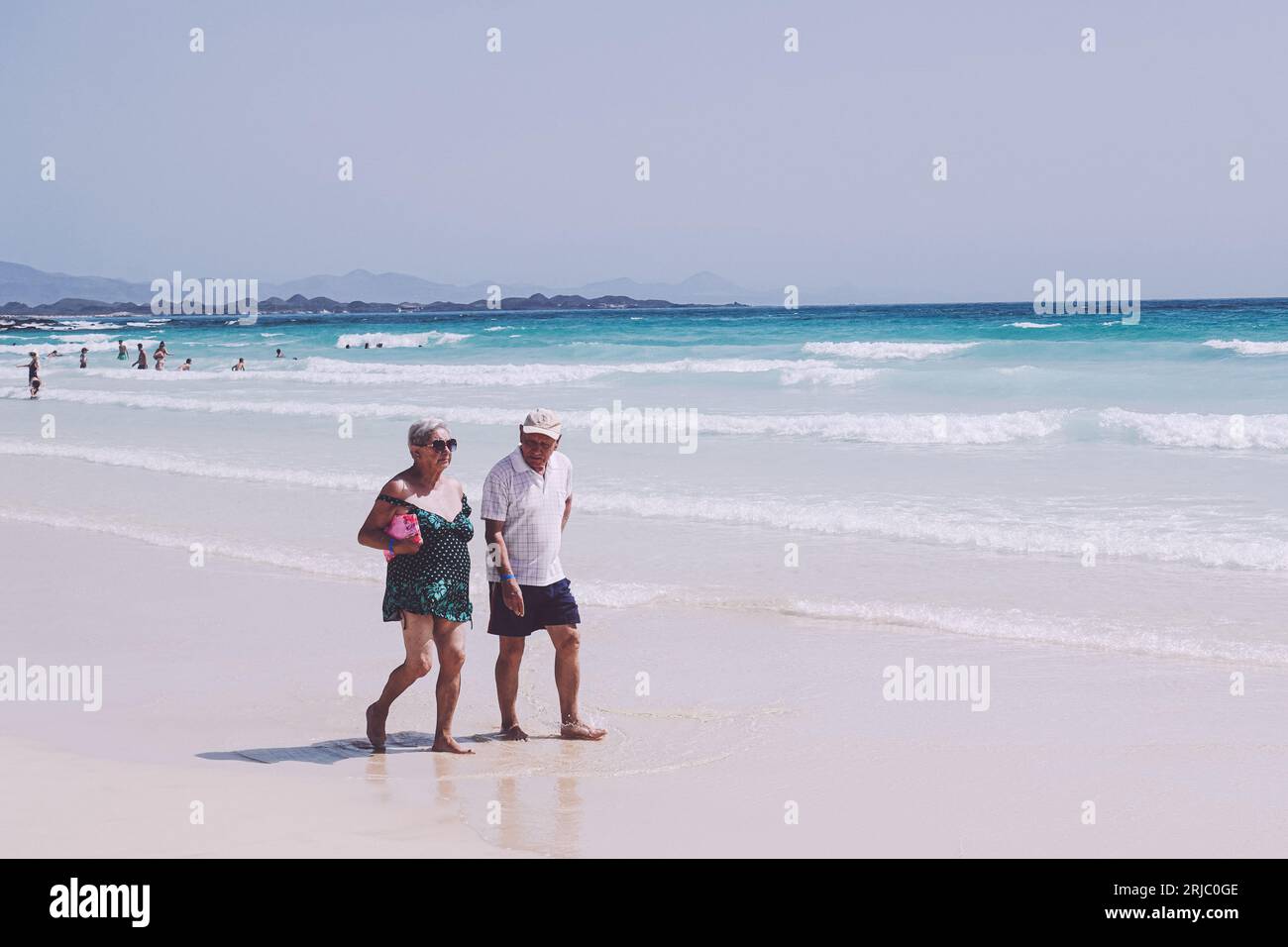 coppia anziana che cammina lungo una spiaggia sabbiosa. in amore e forse in vacanza come parte del loro pensionamento Foto Stock