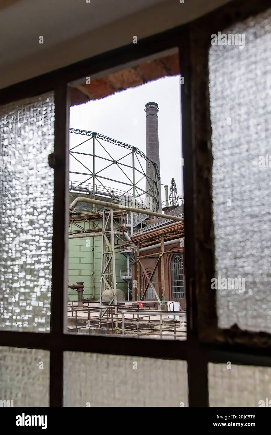 Edifici, attrezzature e sistemi di tubazioni di acciaieria industriale abbandonata e fatiscente nel Landschaftspark pubblico, Duisburg visto attraverso un'apertura Foto Stock