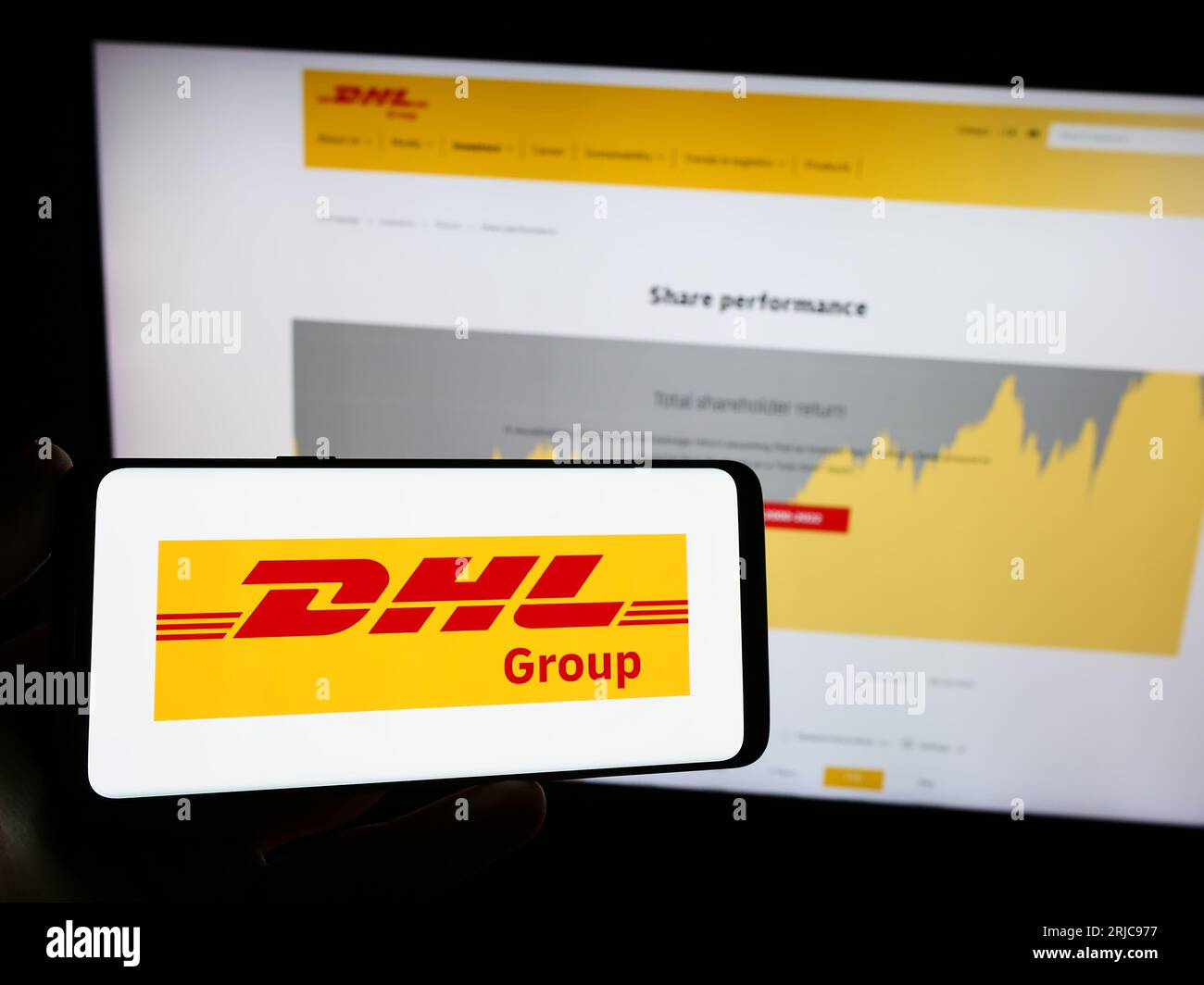 Persona che possiede un telefono cellulare con il logo della società di logistica Deutsche Post AG (gruppo DHL) sullo schermo davanti alla pagina Web. Concentrarsi sul display del telefono. Foto Stock