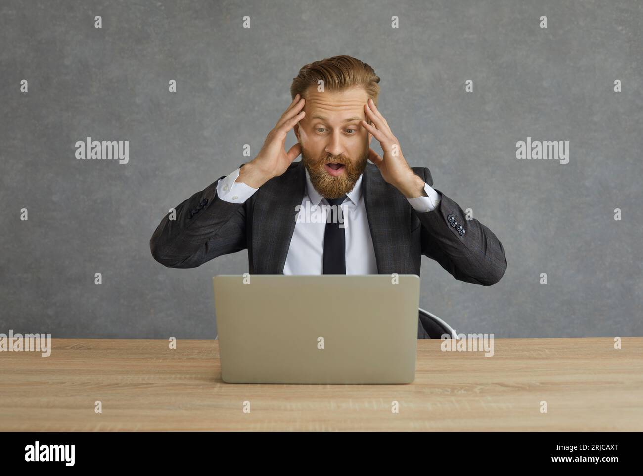 Un uomo d'affari caucasico scioccato e confuso afferra la testa mentre guarda lo schermo del notebook. Foto Stock