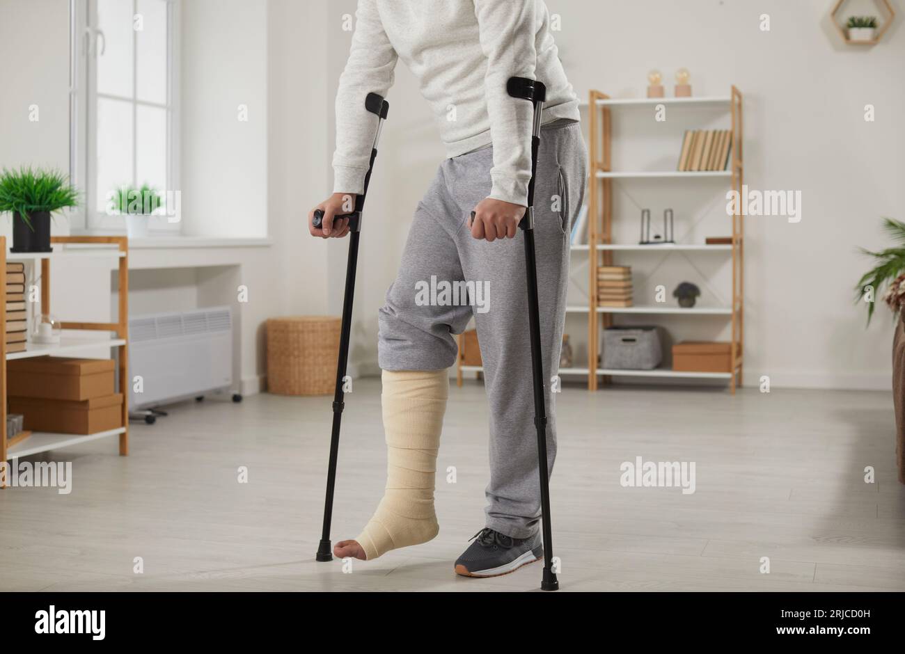 Il tizio è in piedi in salotto su stampelle con gamba bendata. Foto Stock