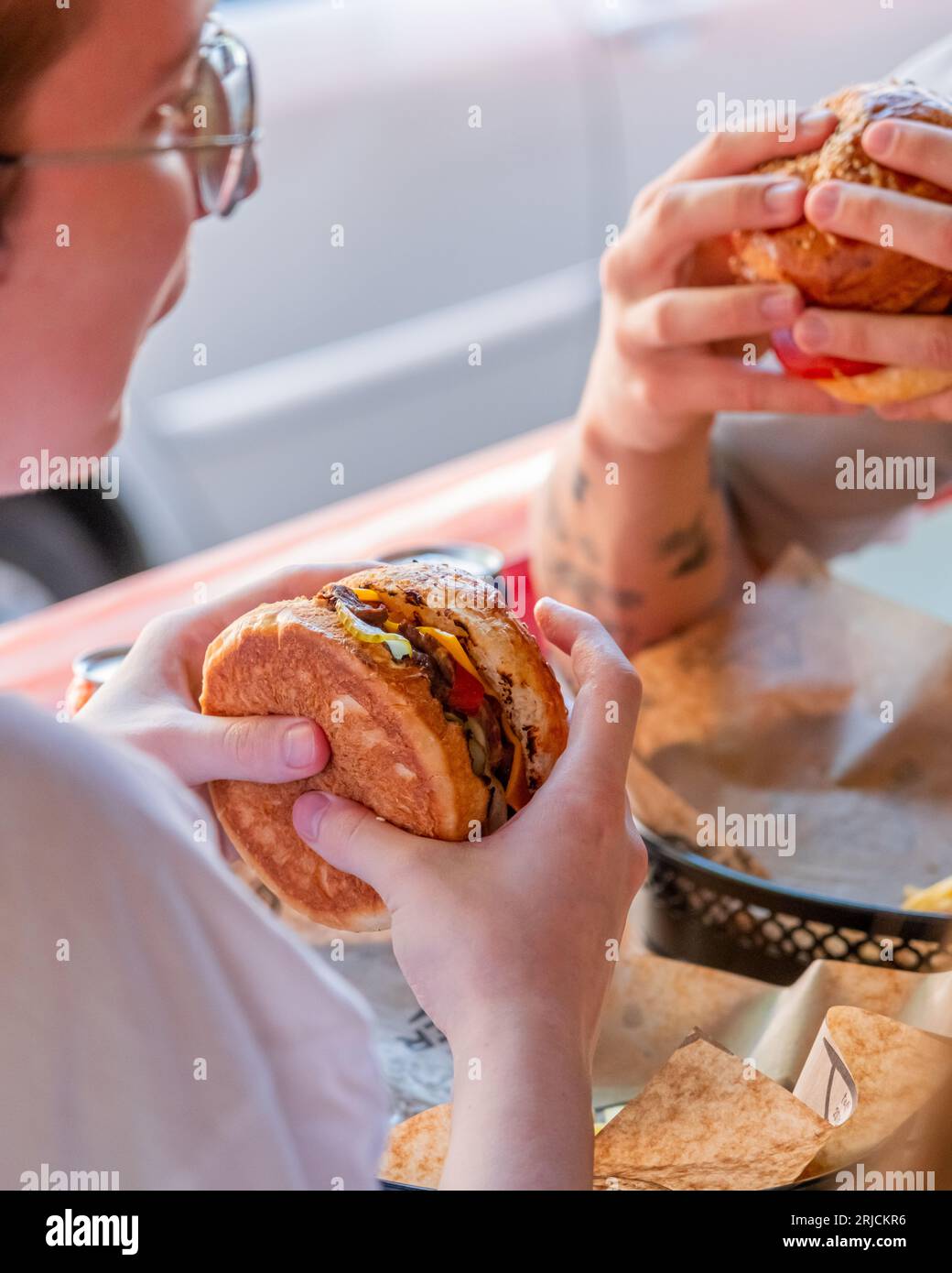 Due uomini che comunicano tra loro e pranzano con hamburger al ristorante. Foto Stock