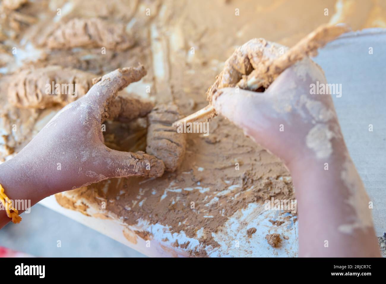 Primo piano sulla modellazione di bambini in argilla naturale con attrezzi manuali durante la lezione di ceramica Foto Stock