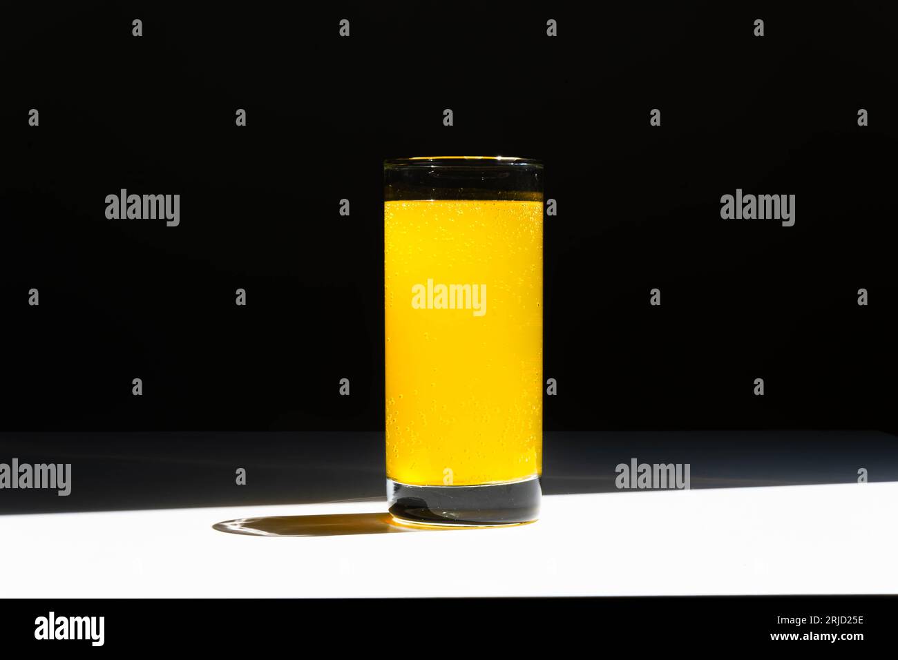 Un bicchiere di acqua vitaminica con bolle su un tavolo bianco e sfondo nero Foto Stock