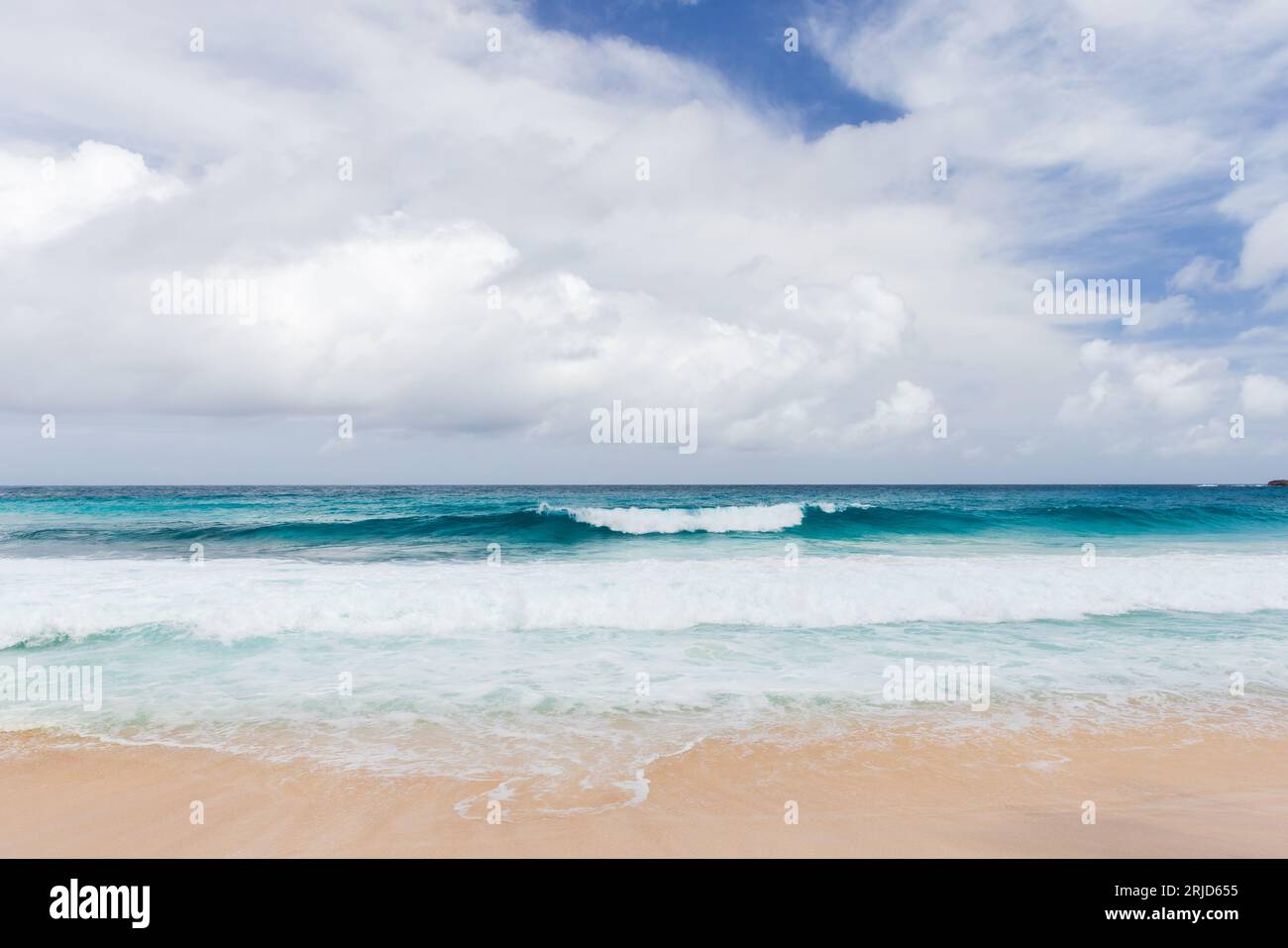 Le onde della costa e la sabbia bianca sono sotto il cielo nuvoloso. Foto del paesaggio della costa oceanica scattata a Anse Intendance Beach, isola di Mahe, Seychelles Foto Stock