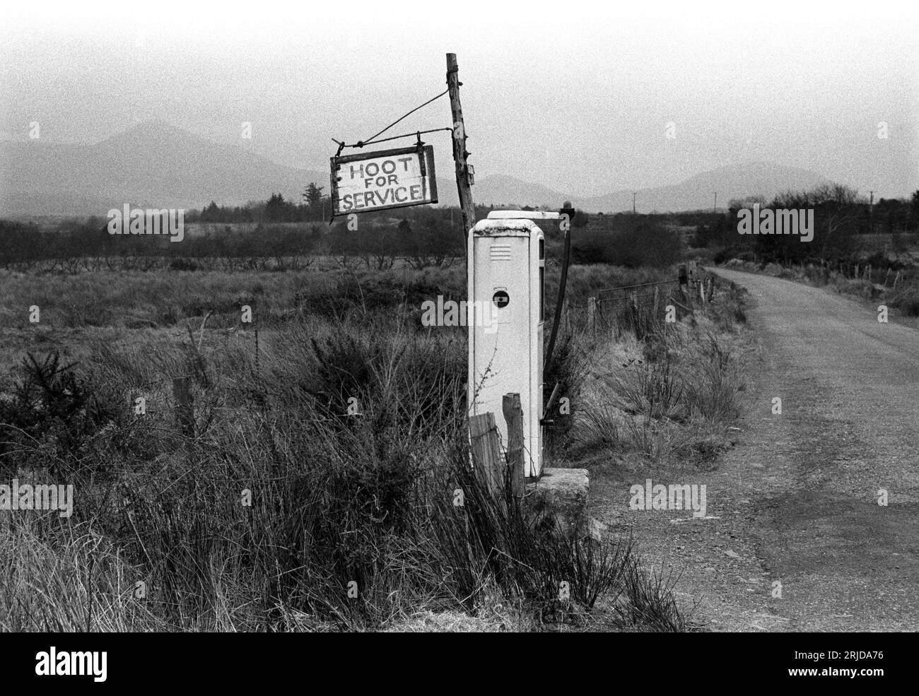 Cartello del distributore di benzina rurale in Countryside Hoot per Service 1970s Eire. L'agricoltore che gestisce il distributore di benzina ascoltando il clacson dell'auto è sceso dal cottage a due o trecento metri di distanza per riempire l'auto. Contea di Kerry, Eire, circa 1972. HOMER SYKES Foto Stock