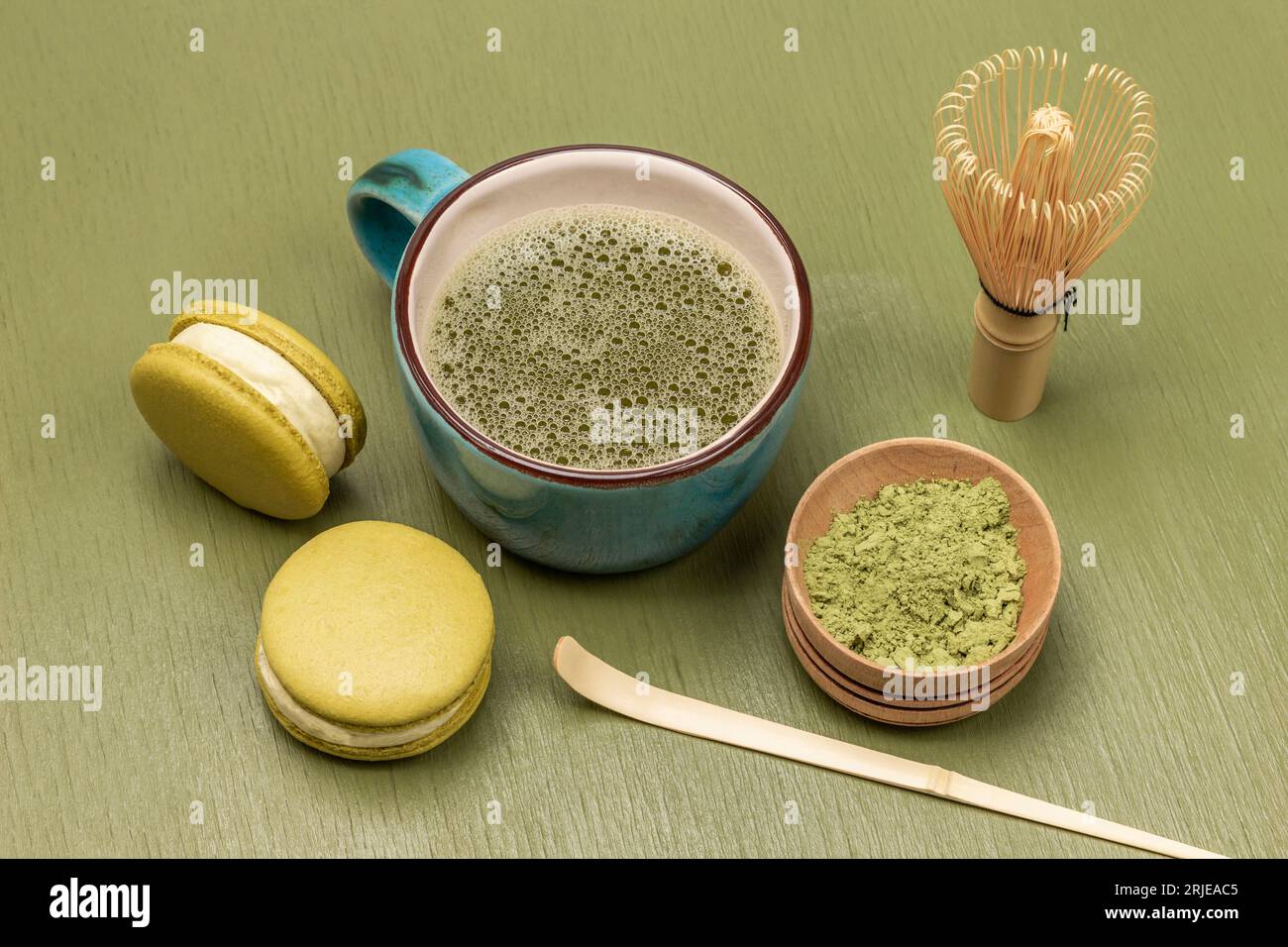 Torta macaron e tazza di tè Matcha. Frullare, cucchiaio di bambù e tè Matcha in polvere in un recipiente di legno. Vista dall'alto. Sfondo verde Foto Stock