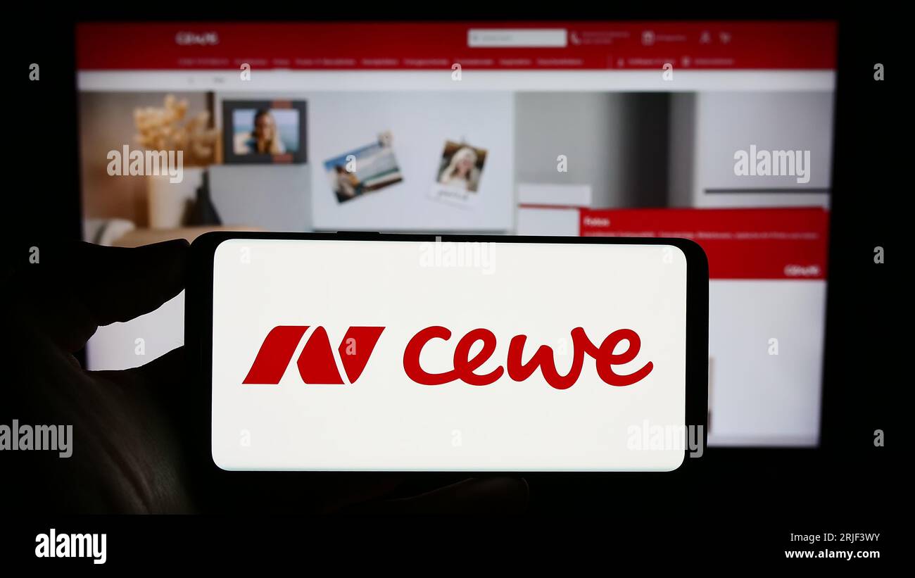Persona che possiede il cellulare con il logo della società di stampa CEWE Stiftung Co. KGaA sullo schermo di fronte alla pagina Web aziendale. Concentrarsi sul display del telefono. Foto Stock
