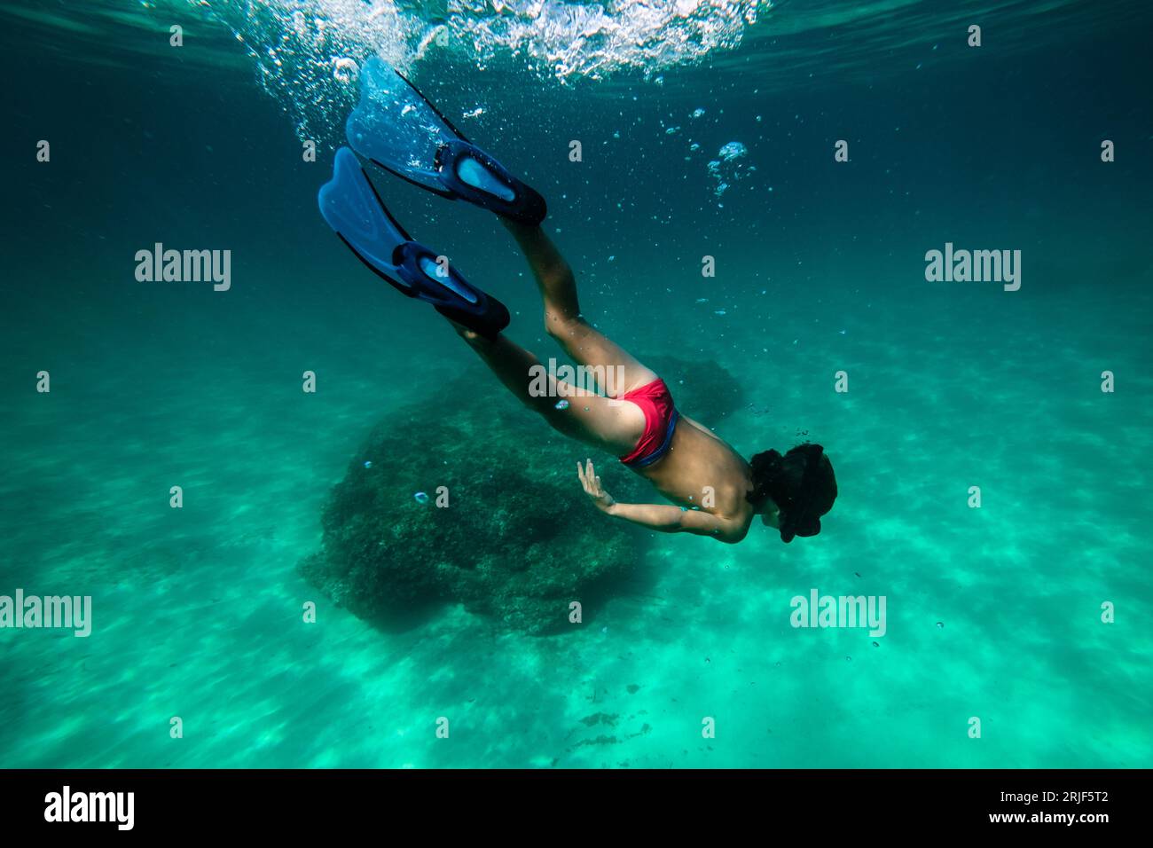 Corpo completo di giovane subacqueo anonimo con maschera da snorkeling e pinne che nuotano sott'acqua ed esplorano la barriera corallina e l'ecosistema del fondo marino Foto Stock