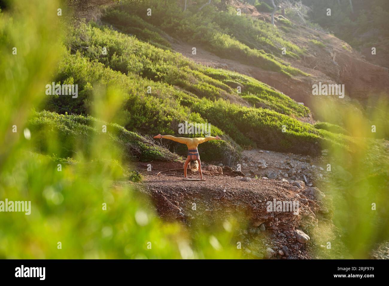 Vista posteriore di una giovane donna anonima in abbigliamento sportivo che fa la spaccatura delle gambe mentre prende Adho Mukha Vrikshasana posa in natura Foto Stock