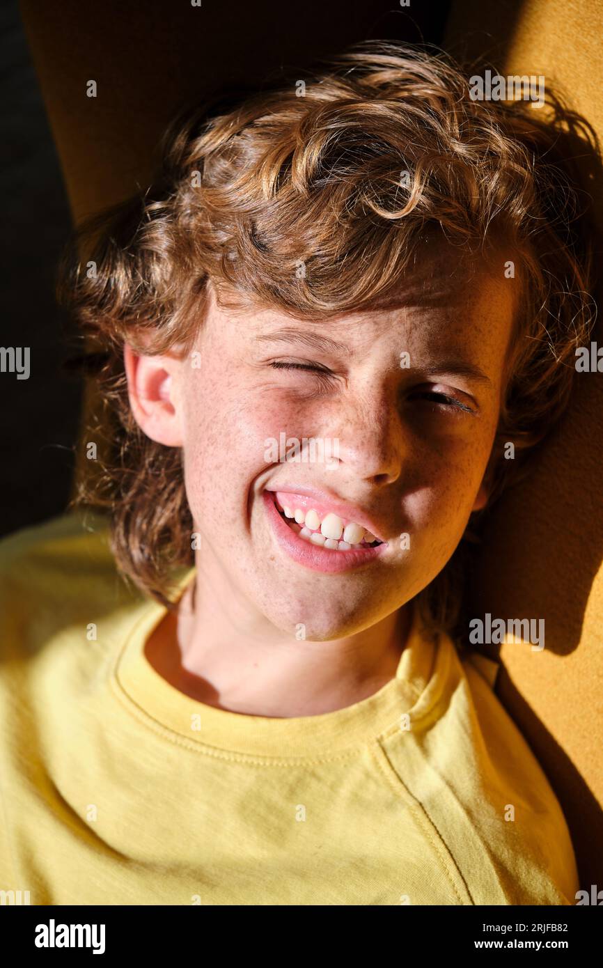 Bambino allegro con le frettole in abbigliamento giallo che fa il viso mentre si guarda la fotocamera alla luce del sole Foto Stock