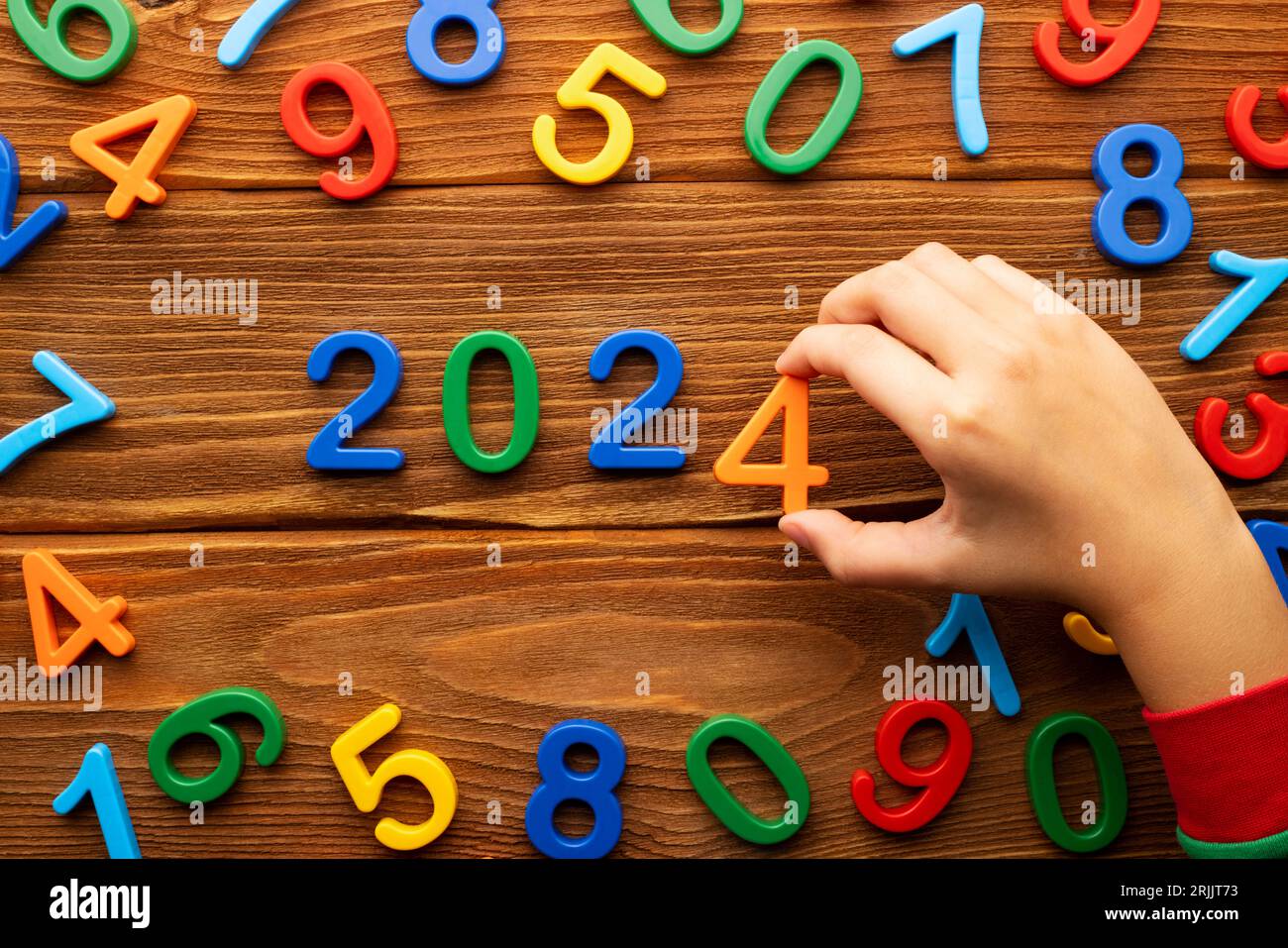 Il bambino compone l'anno 2024 da numeri multicolori su uno sfondo di legno Foto Stock