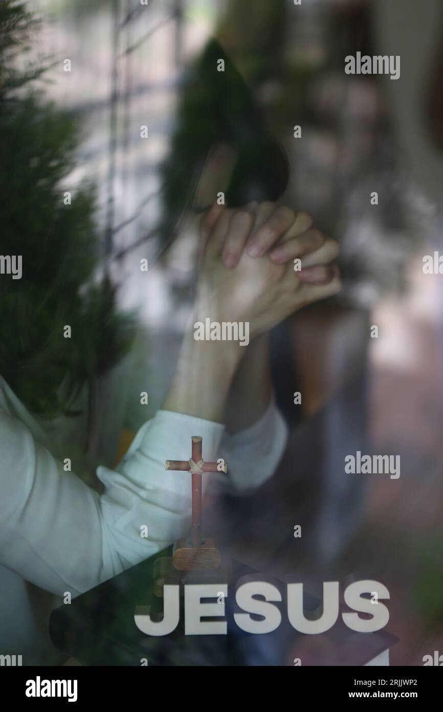 Donna cristiana della chiesa che prega e predica con le mani insieme, libro biblico e Santa croce di Gesù Cristo riflessa nella finestra Foto Stock