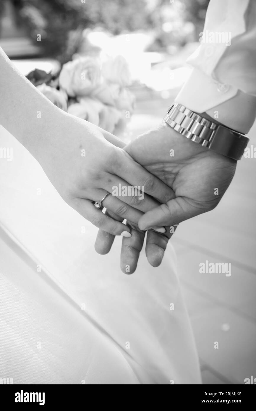 Un primo piano in scala di grigi di una coppia sposata che si tiene per mano. Foto Stock