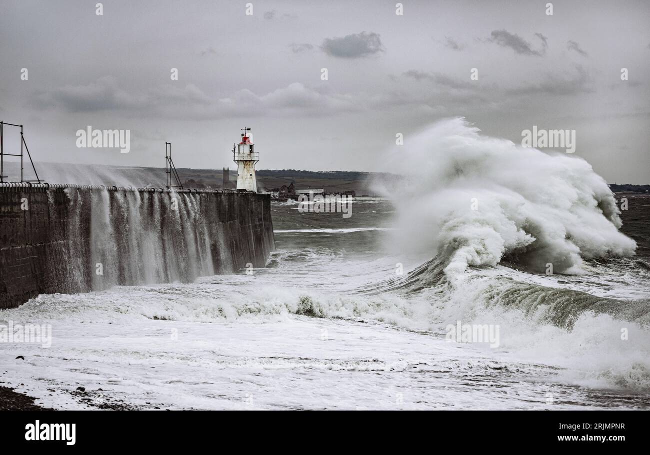 Enormi onde si infrangono nel porto di Newlyn, alcune delle quali raggiungono l'altezza e sopra il faro che si trova sulla parete del porto. Newlyn, Cornovaglia, Regno Unito Foto Stock
