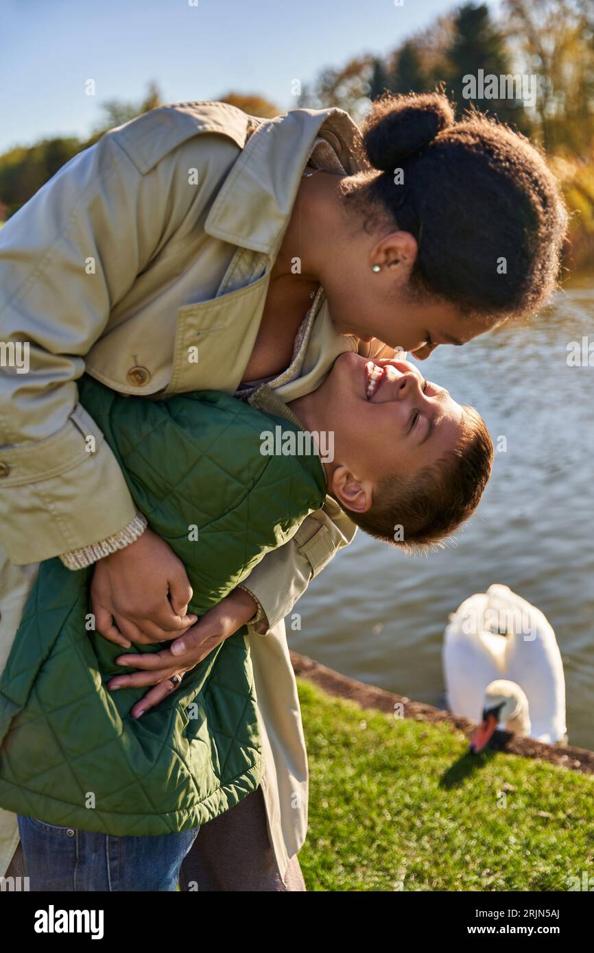 legame familiare, amore, madre e bambino afroamericani felici che abbracciano vicino al lago, natura, autunno, divertimento Foto Stock