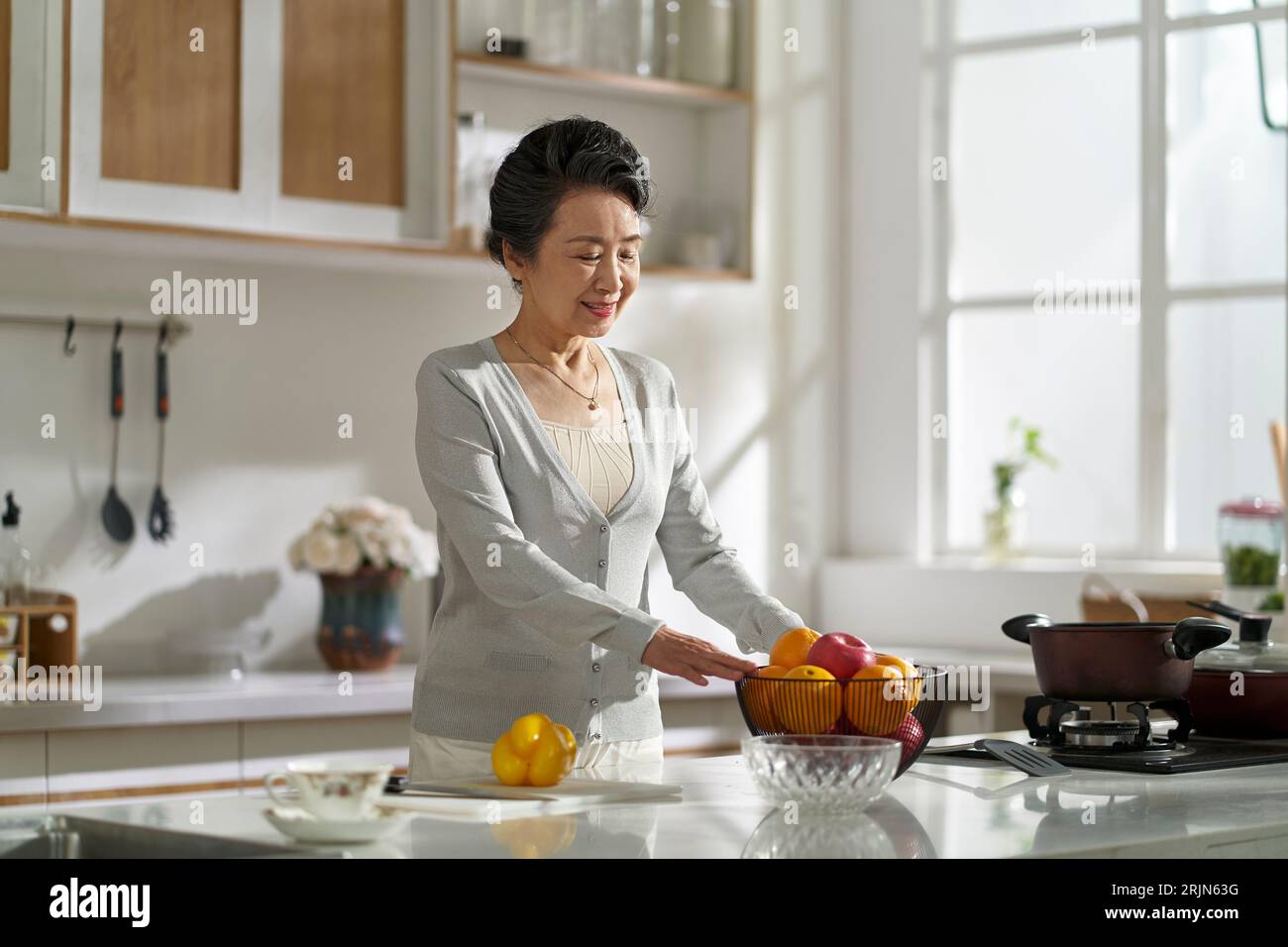donna asiatica anziana in piedi in cucina moderna a casa preparandosi a preparare il cibo Foto Stock