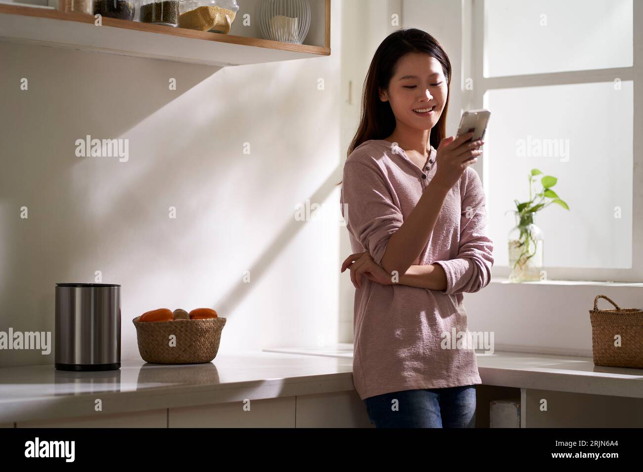 bella giovane donna asiatica in piedi in cucina a casa usando il cellulare Foto Stock