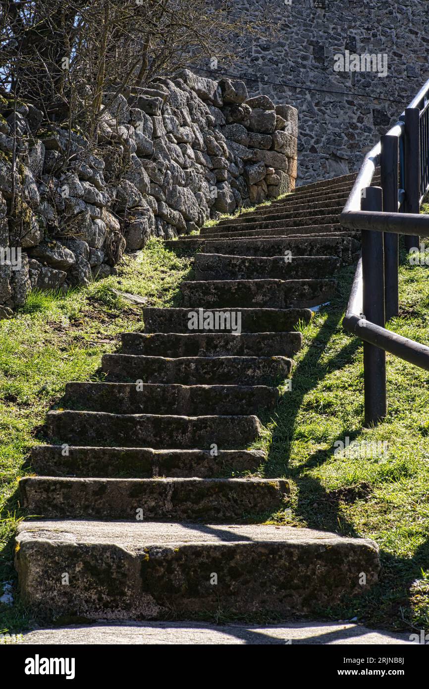 Una scena all'aperto con scale che salgono su un muro di pietra, con erba verde in primo piano. Foto Stock
