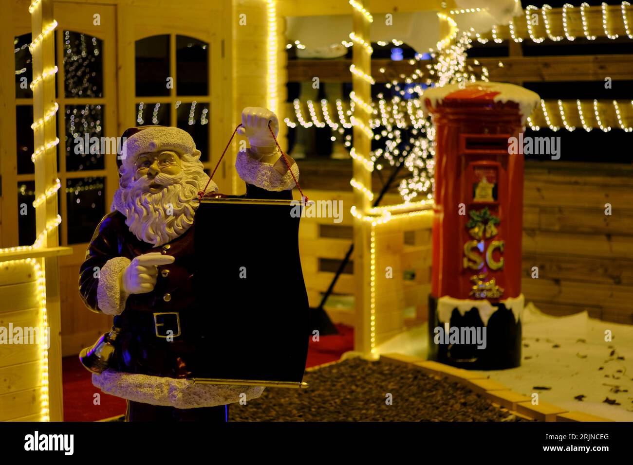 Una figura festosa di Babbo Natale illuminata da luci di Natale che tengono in mano una scatola Foto Stock