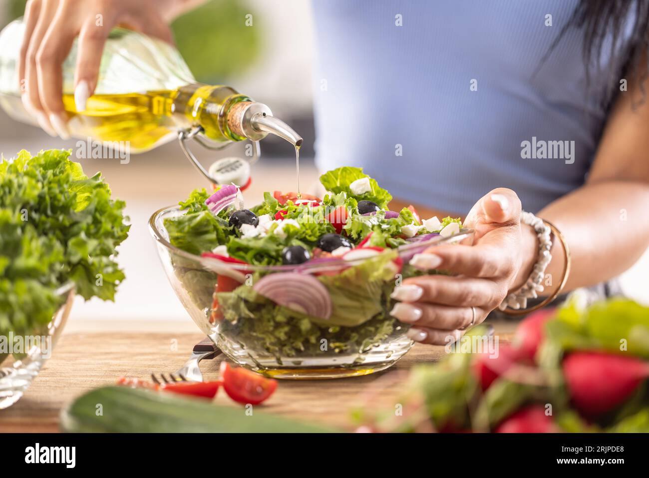 La preparazione finale di un'insalata sana e alla fine la donna versa l'olio d'oliva. Foto Stock