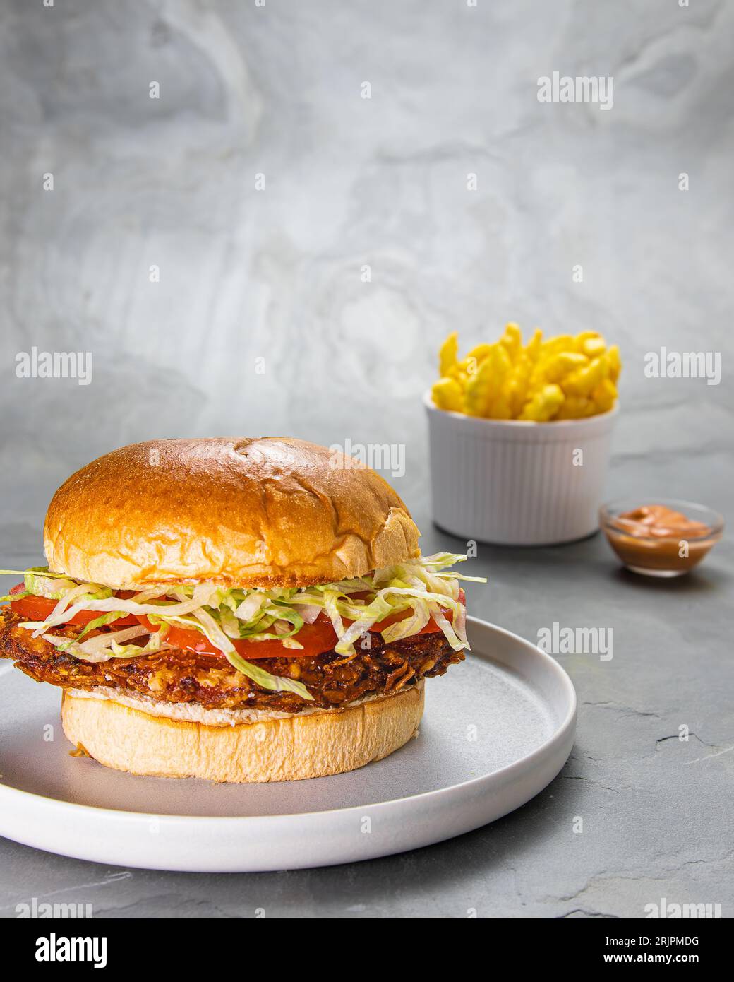 Primo piano di un hamburger di filetto di pollo croccante servito con patatine fritte su sfondo grigio Foto Stock