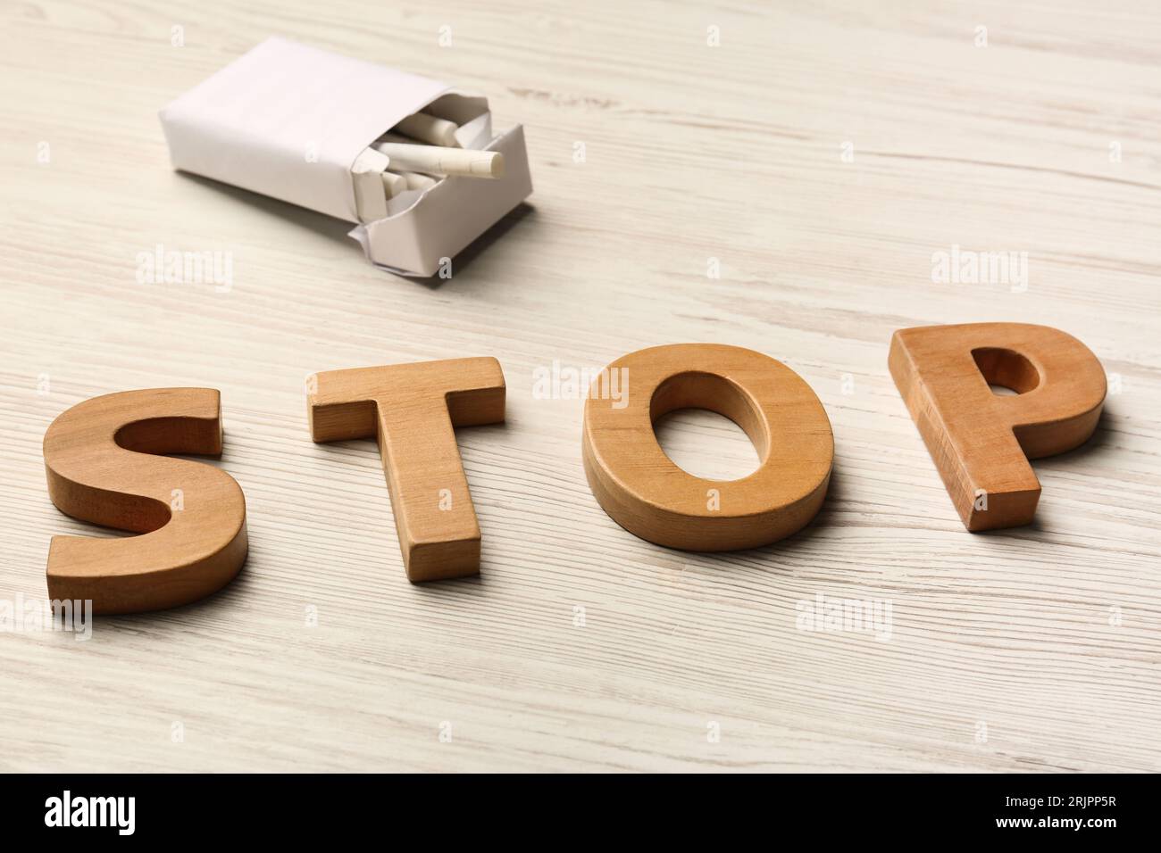 Confezione con sigarette e parola Stop fatta di lettere su un tavolo di legno bianco. Divieto di fumo Foto Stock