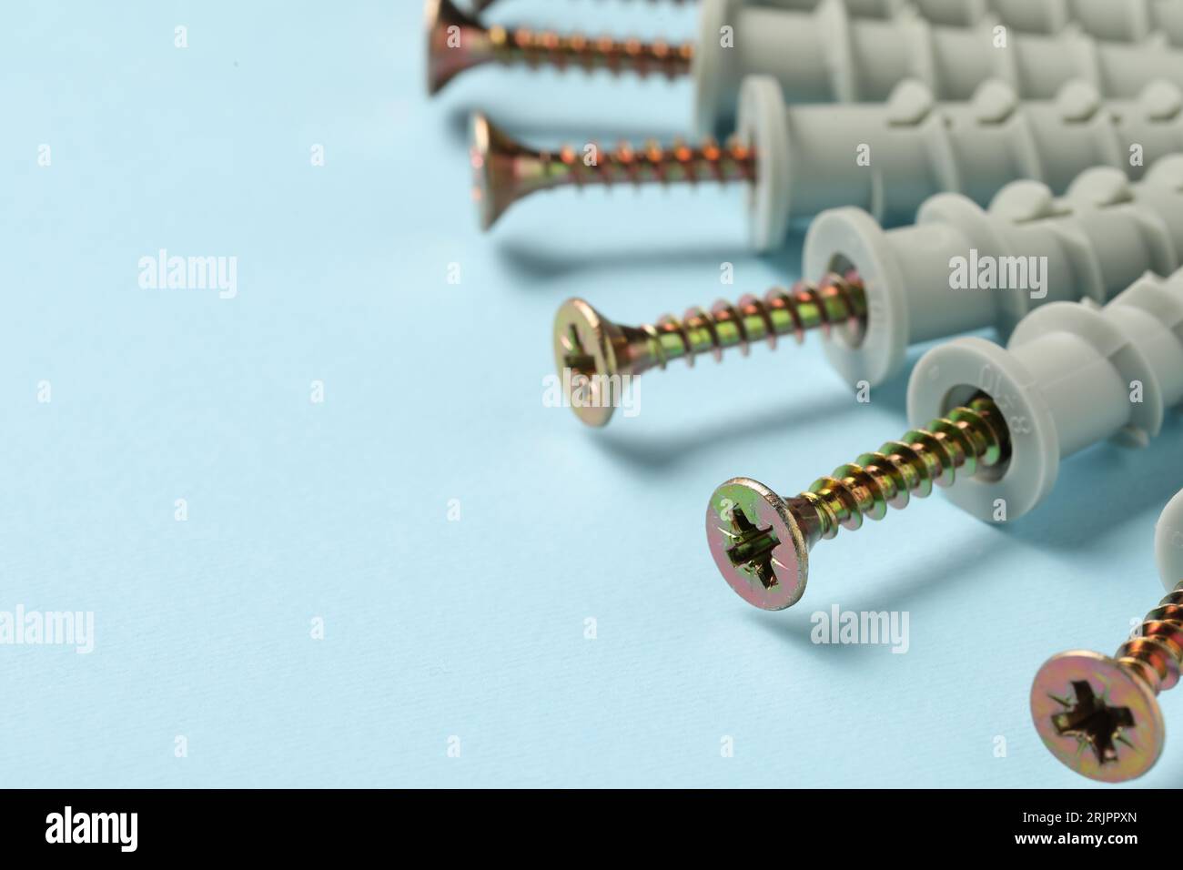 Molte viti metalliche con tasselli su sfondo azzurro, primo piano. Spazio per il testo Foto Stock