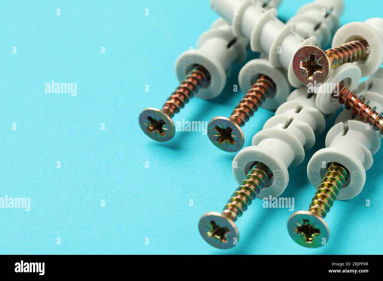 Molte viti metalliche con tasselli su sfondo azzurro, primo piano. Spazio per il testo Foto Stock