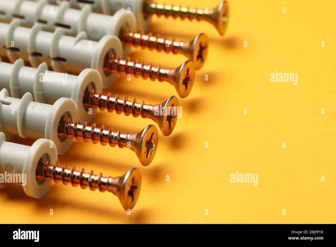 Molte viti metalliche con perni su sfondo arancione, primo piano. Spazio per il testo Foto Stock