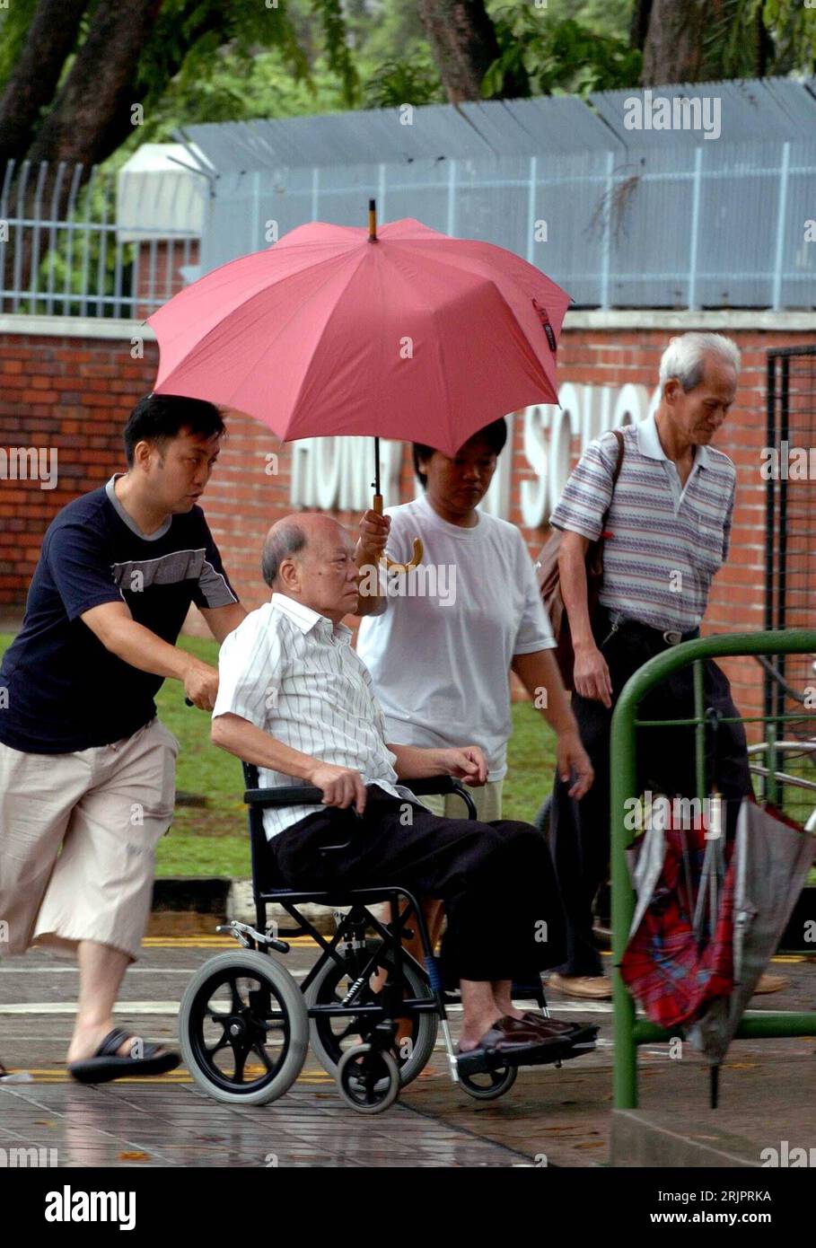 Bildnummer: 51227349 Datum: 06.05.2006 Copyright: imago/Xinhua Rollstuhlfahrer wird von seiner Familie durch den Regen in Singapur geschoben - PUBLICATIONxNOTxINxCHN, Personen; 2006, Singapur, , , , , , , Regenschirm, Regenschirme, Schirm, Schirme, Rollstuhlfahrer, Gehbehinderter, Gehbehinderte, Behinderter, Behinderte, , Rollstuhl, Rollstühle, Regen; , hoch, Kbdig, Gruppenbild, Singapur / Gehbehinderung, Pflege, Fürsorge, Familie, Wetter, Regenwetter, Mann, Männer, alter, alt, alte, senior, Senioren Foto Stock
