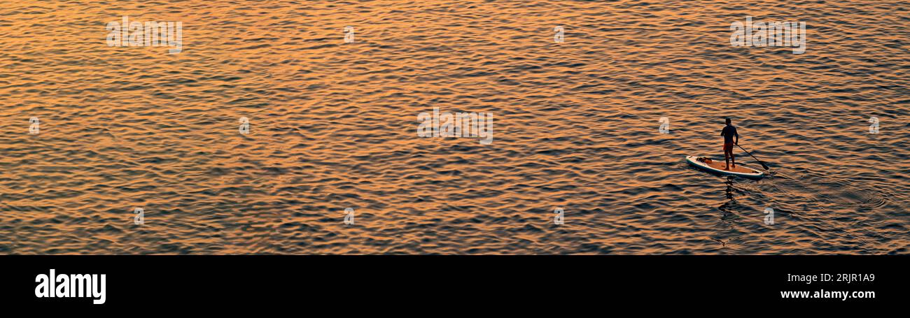 Le persone avventurose su una tavola da paddle stand up stanno pagaiando durante una luminosa e vibrante alba Foto Stock