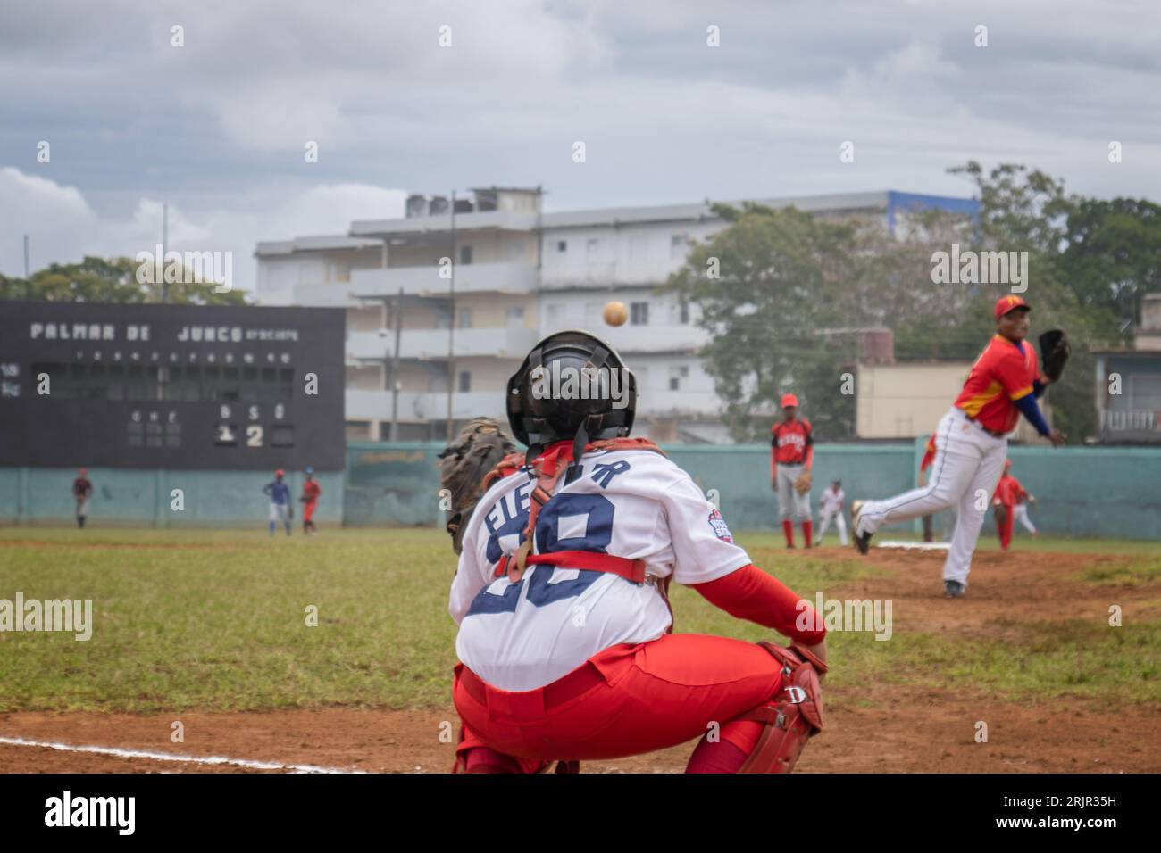 Un giocatore di baseball si trova al piatto di casa, pronto a fare oscillare la mazza, mentre altri giocatori sul campo di diamanti aspettano il campo Foto Stock