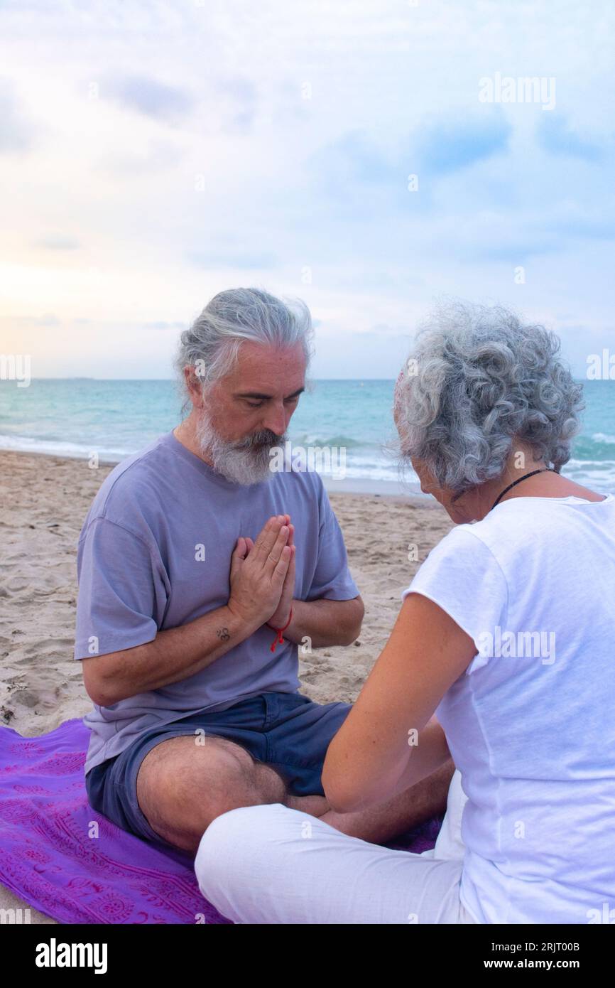 Coppia che meditano insieme in una posizione seduta di preghiera favorendo il rapporto personale sulla spiaggia Foto Stock