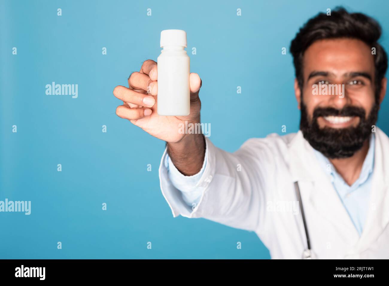 Allegro medico maschio indiano che mostra barattolo di pillole alla fotocamera su sfondo blu studio, messa a fuoco selettiva, mockup Foto Stock