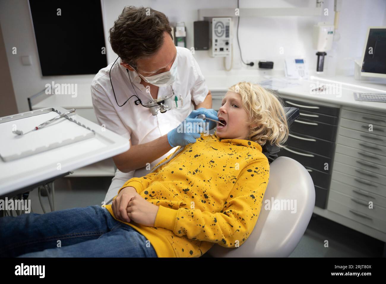 Dentista che esamina i denti del ragazzo biondo in clinica medica Foto Stock