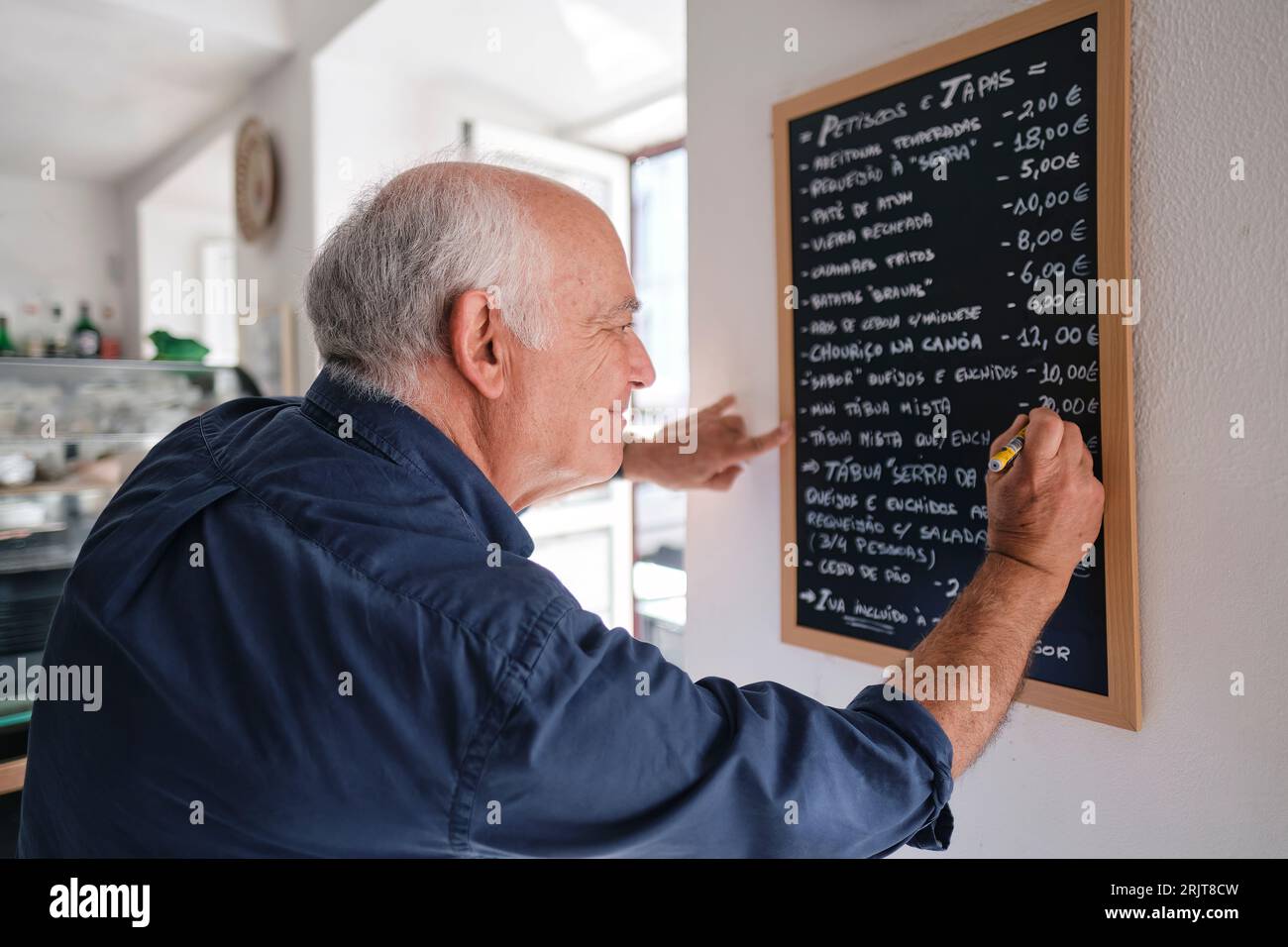 Sorridente proprietario di un caffè che scrive menu su lavagna nera con penna Foto Stock