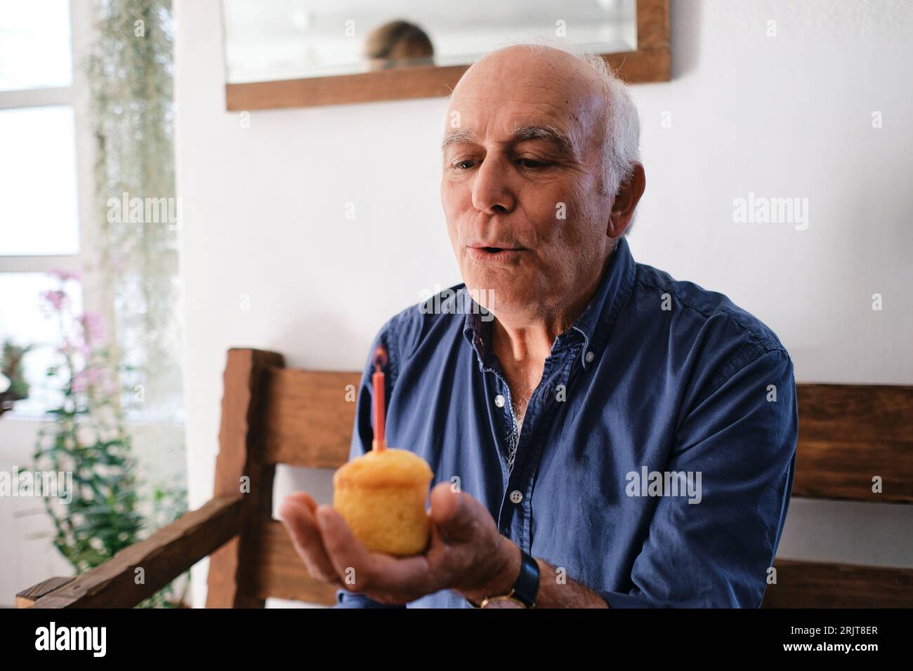 Un uomo anziano che soffia una candela sul cupcake Foto Stock