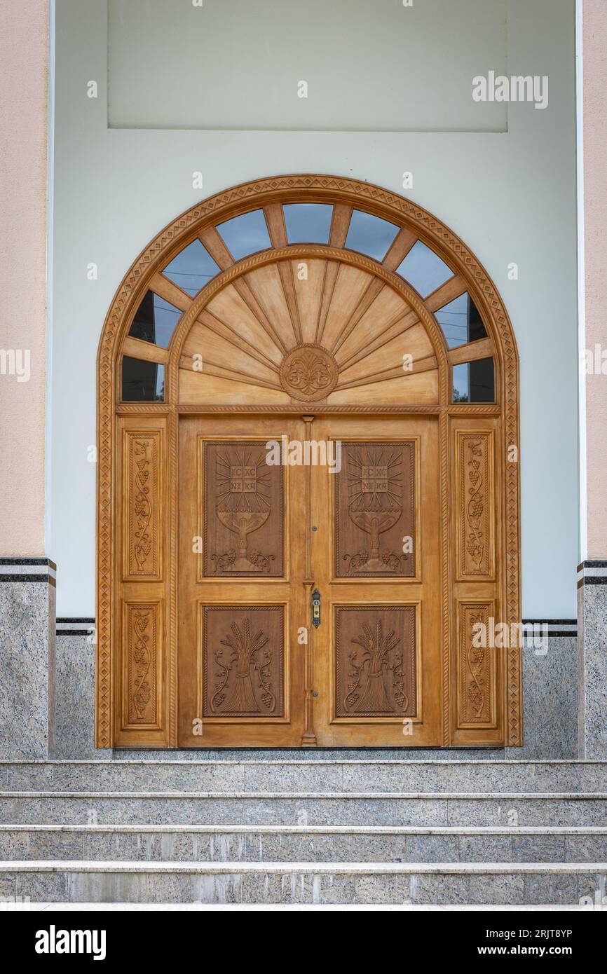 Una vecchia porta in legno dal design intricato con una serie di gradini in cemento che vi conducono Foto Stock