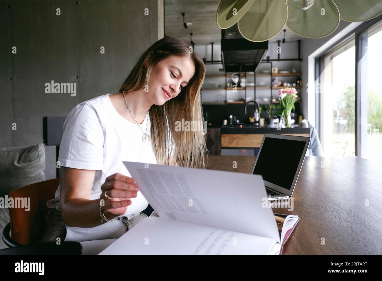 Freelance sorridente che gira pagina di libro a casa Foto Stock