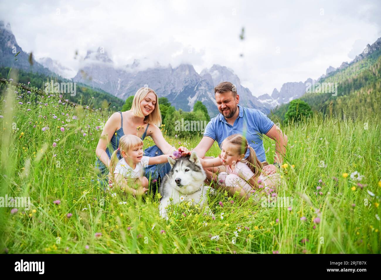 La famiglia si sta divertendo in vacanza con il cane seduto sull'erba davanti alle montagne Foto Stock