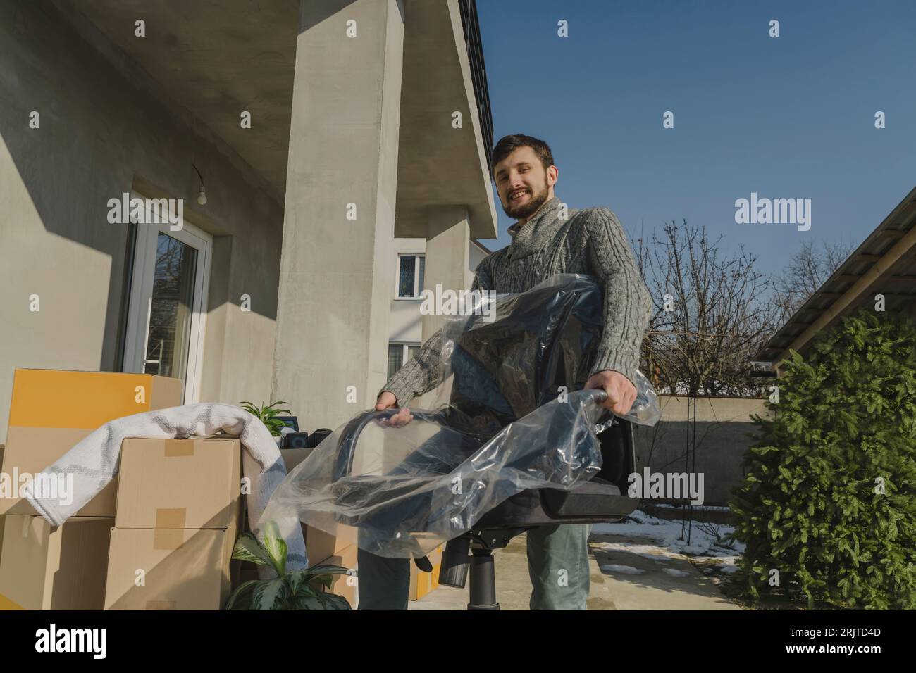 Uomo sorridente che porta la sedia avvolta in una nuova casa Foto Stock