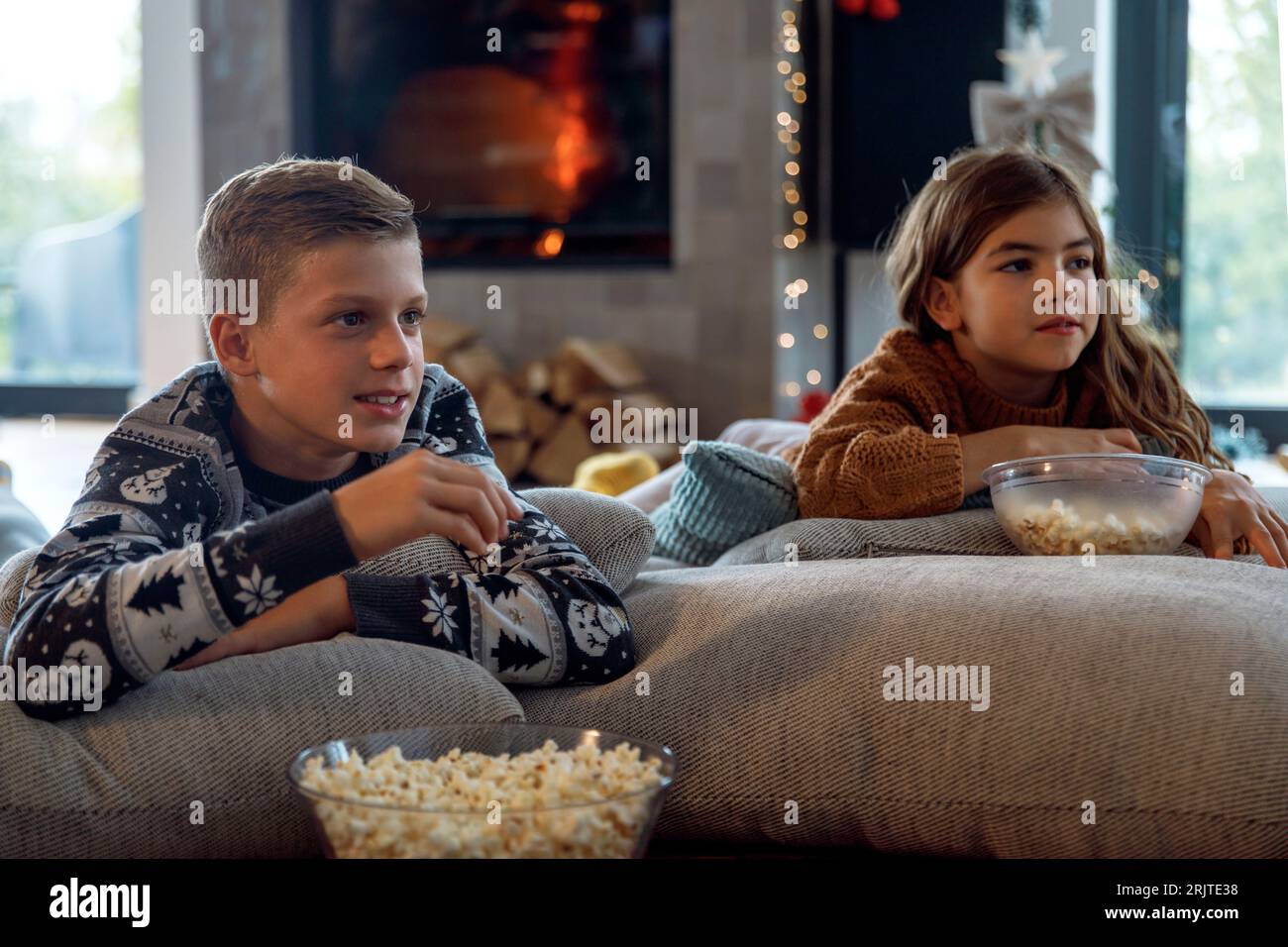 Fratello e sorella che bevono popcorn e guardano la TV in salotto Foto Stock