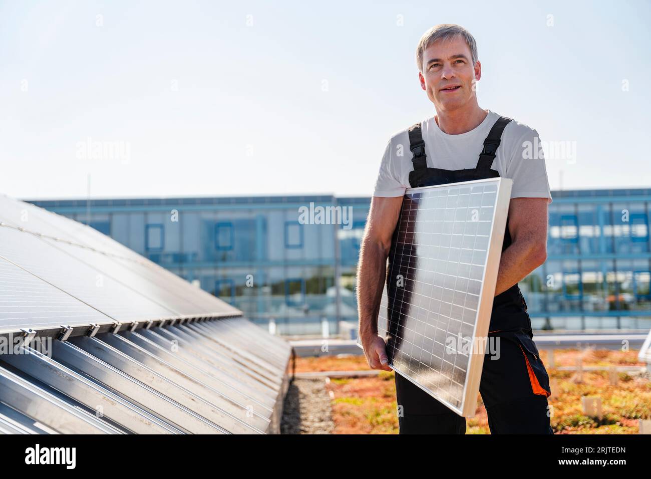 Artigiano che tiene pannelli solari sul tetto di un edificio aziendale Foto Stock