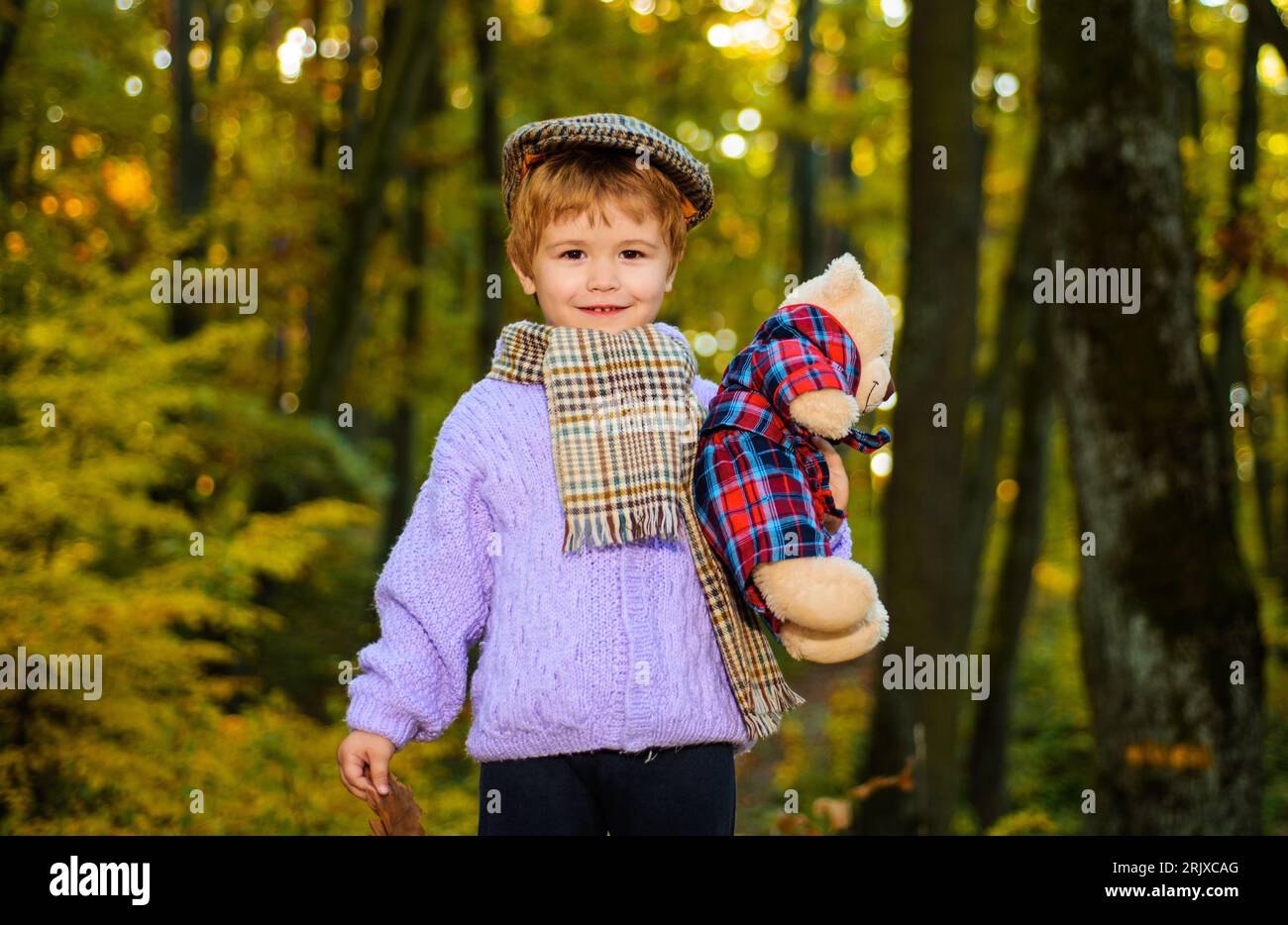 Bambino sorridente nella foresta autunnale. Il bambino in abiti autunnali gioca con l'orsacchiotto nel parco. Bambino che gioca nella foresta autunnale con orsacchiotto Foto Stock