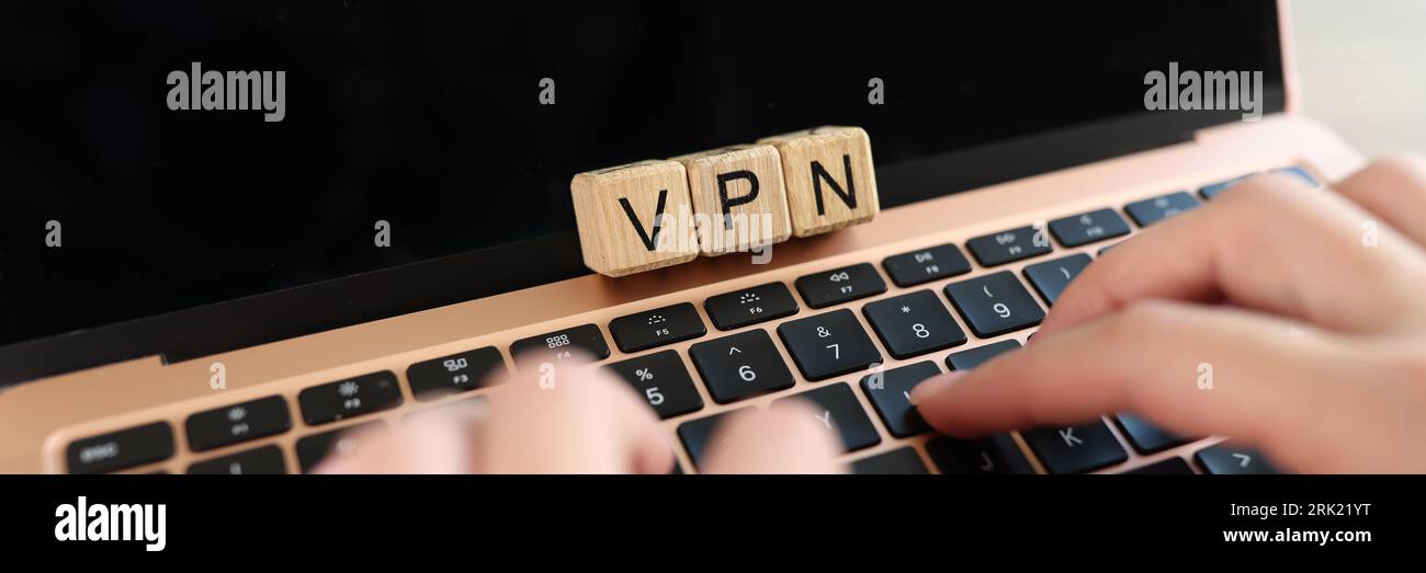 Mani utente che digita sulla tastiera del computer portatile con parola VPN su cubi di legno primo piano. Foto Stock
