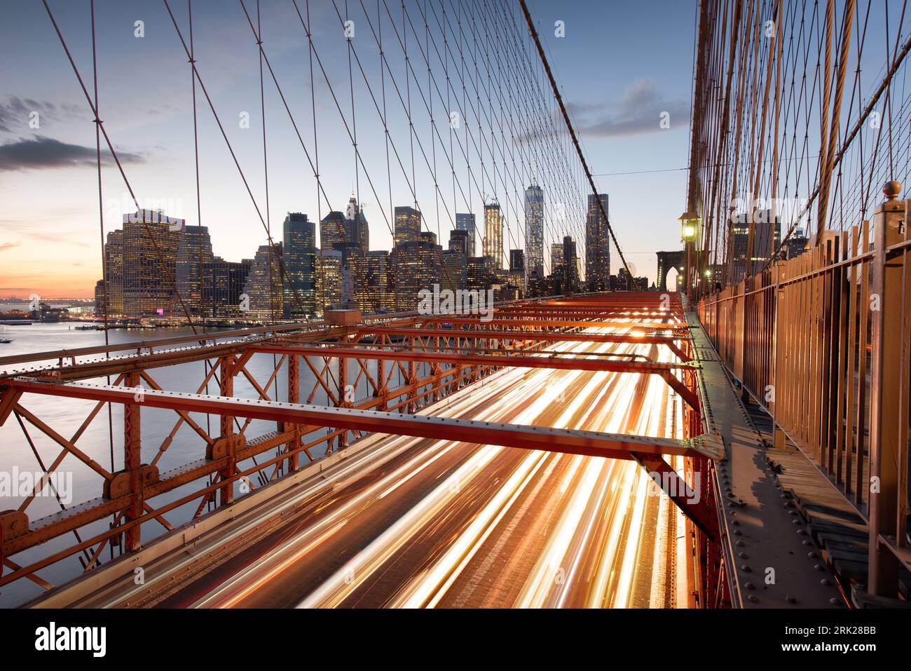 La vista del quartiere finanziario di New York City dietro il traffico sul Ponte di Brooklyn dopo il tramonto. Foto Stock