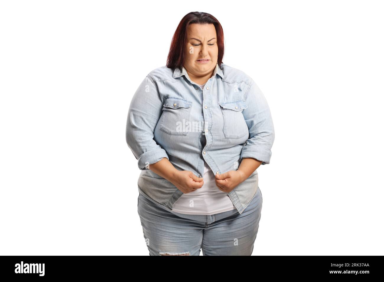 Donna in sovrappeso che cerca di infilarsi una camicia in denim isolata su sfondo bianco Foto Stock