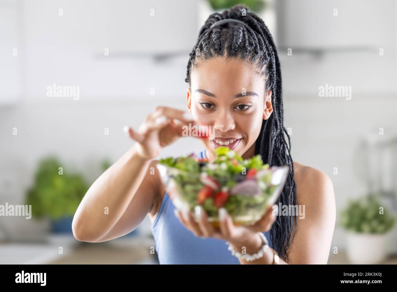 Giovane donna afroamericana prepara insalata sana, aggiunge pomodori. Foto Stock