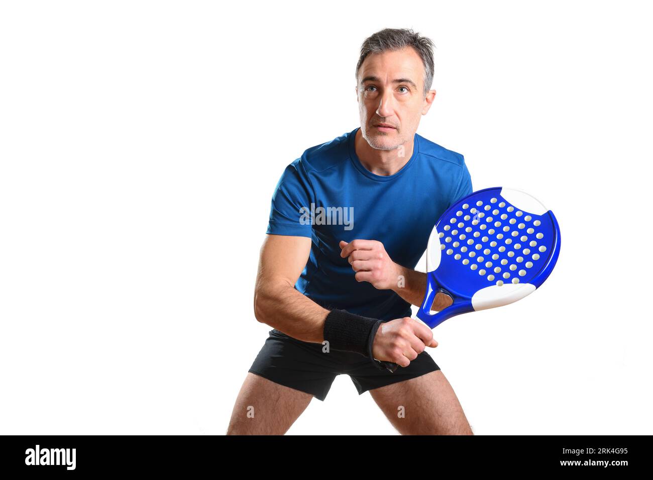 Ritratto di un uomo che gioca a PADEL tennis in posizione per colpire una palla rovescia indossando abiti sportivi blu e neri e sfondo bianco isolato. Vista frontale Foto Stock
